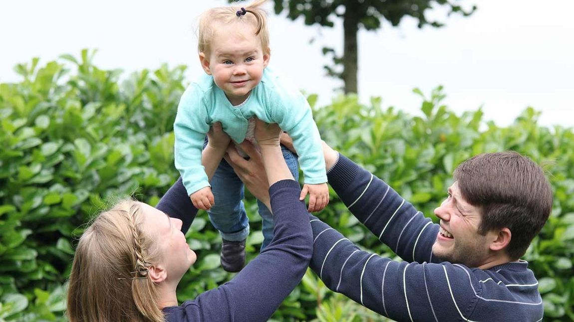 Junge Eltern heben ihre einjährige Tochter in die Luft.